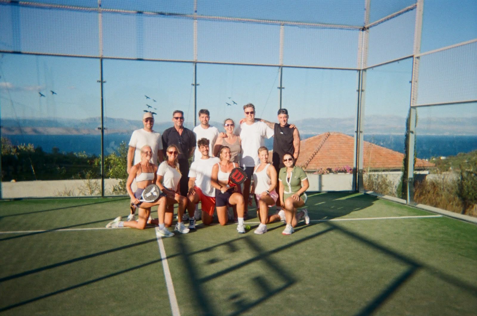 The whole group together on court, sea behind the glass